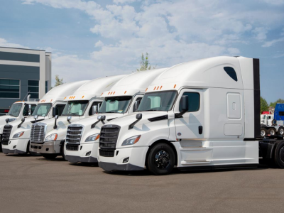 fleet of 5 white semi trucks parked in a parking lot